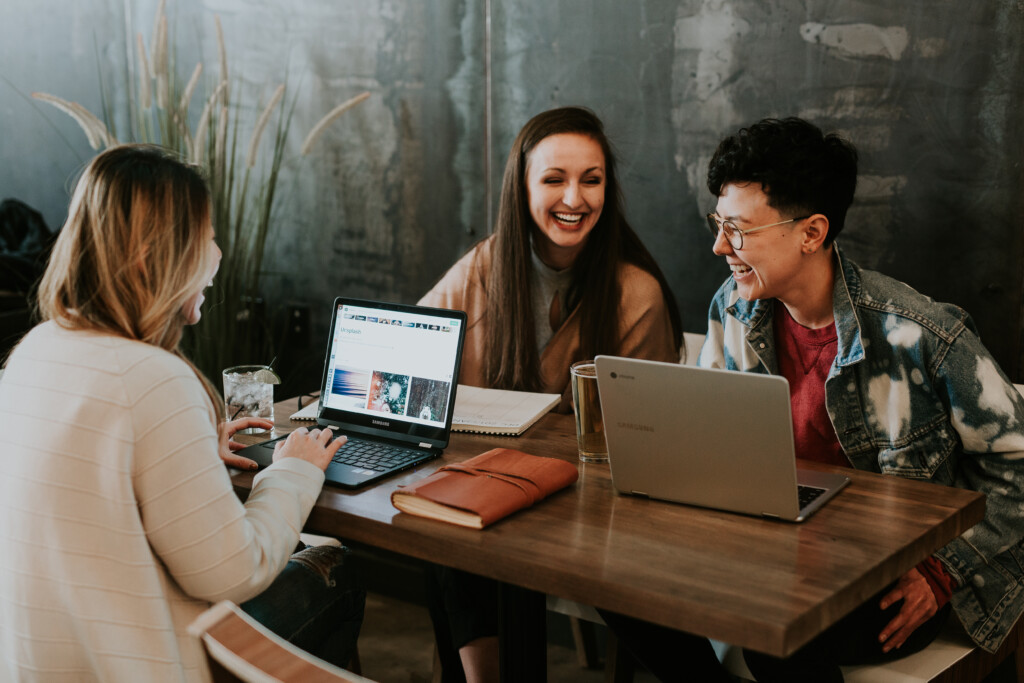 three young people sitting around a table with laptops